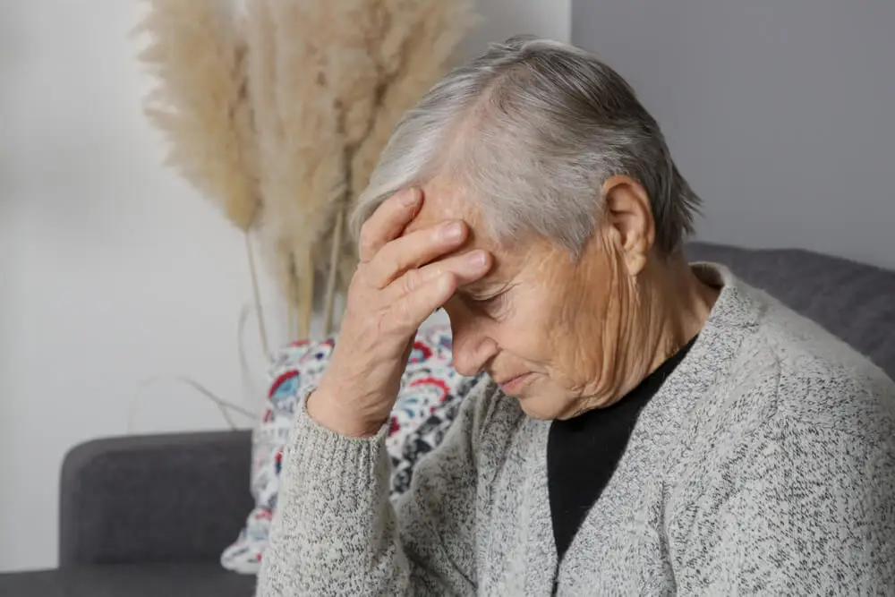 Mujer mayor con tristeza y manos en la frente.