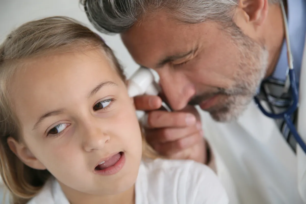 Médico examina oído de niña.