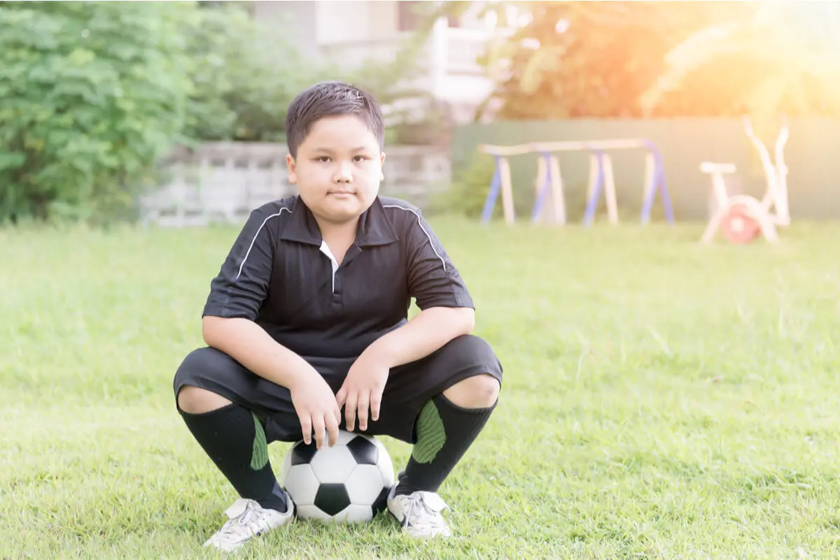 Idealgewicht für Kinder - übergewichtiger Junge sitzt auf einem Fußball