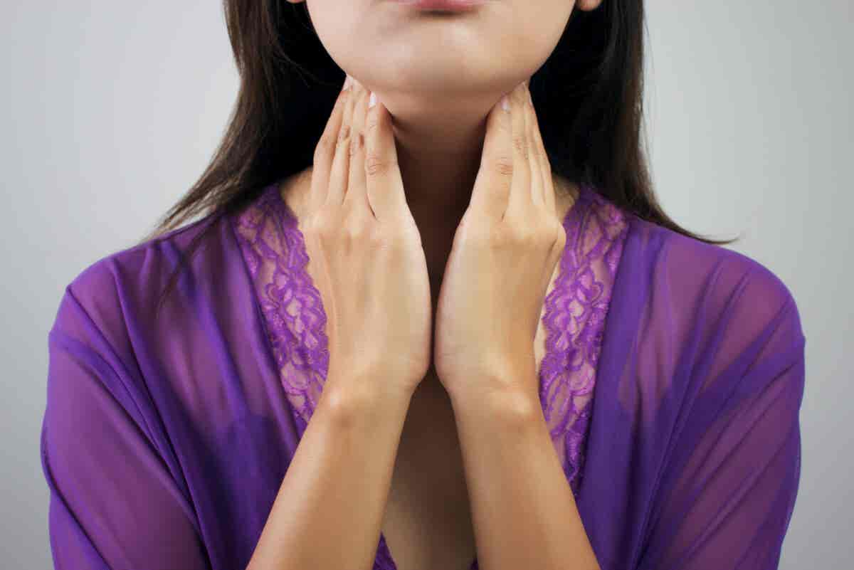 Mujer toca su tiroides en el cuello