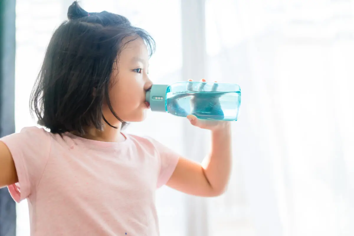 Niña bebe agua y se hidrata.