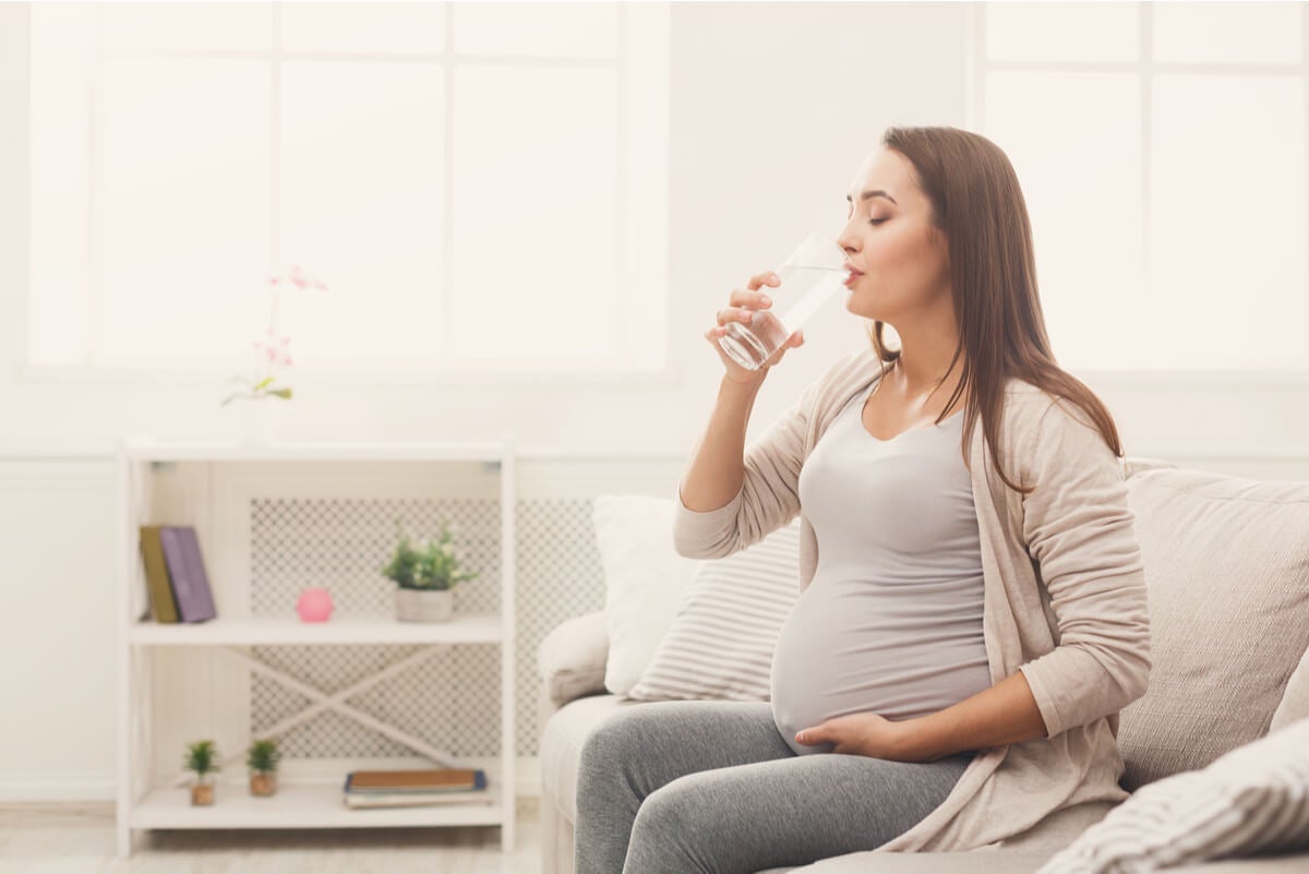 Mujer embarazada toma agua.
