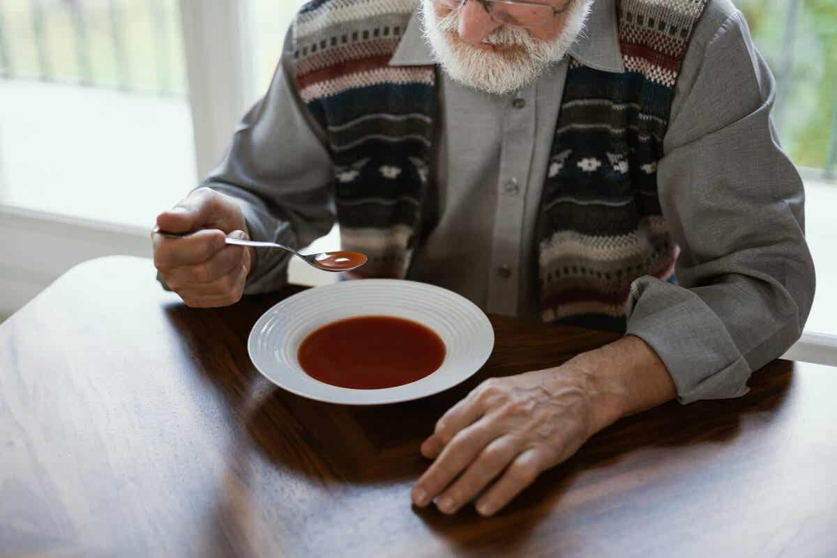 Anciano con párkinson cenando.