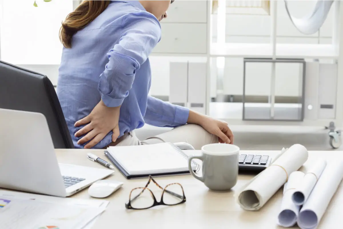 akute Lumbago - Frau mit Kreuzschmerzen am Schreibtisch