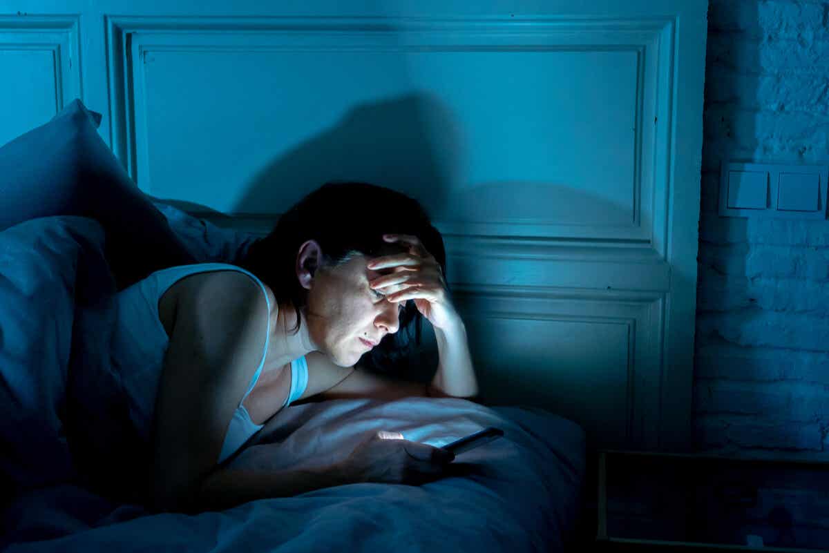Mujer lee celular durante la noche en la cama.