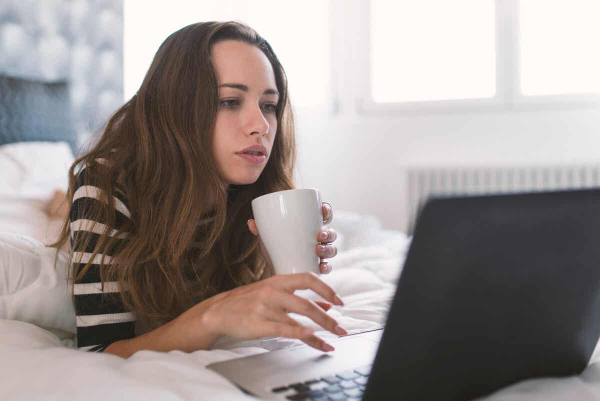 Mujer trabaja desde la casa en su cama con un ordenador.