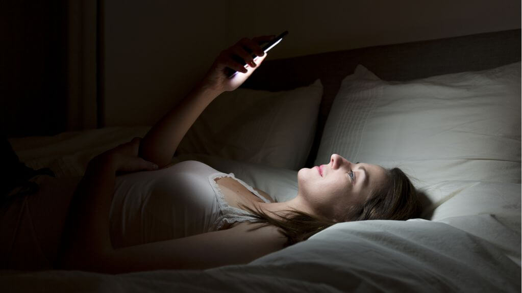 Mujer con el móvil en la cama antes de dormir.