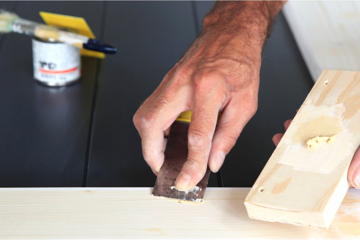 Lack von Holz entfernen - Mann schabt Lackreste mit einem Spatel ab