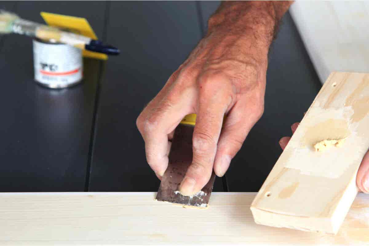 Lack von Holz entfernen - Mann schabt Lackreste mit einem Spatel ab