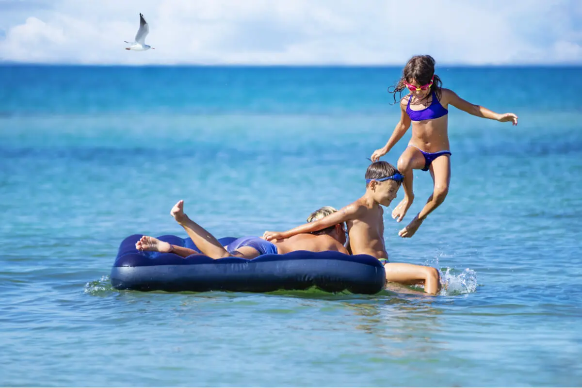 Niños juegan en colchón inflable en el agua.