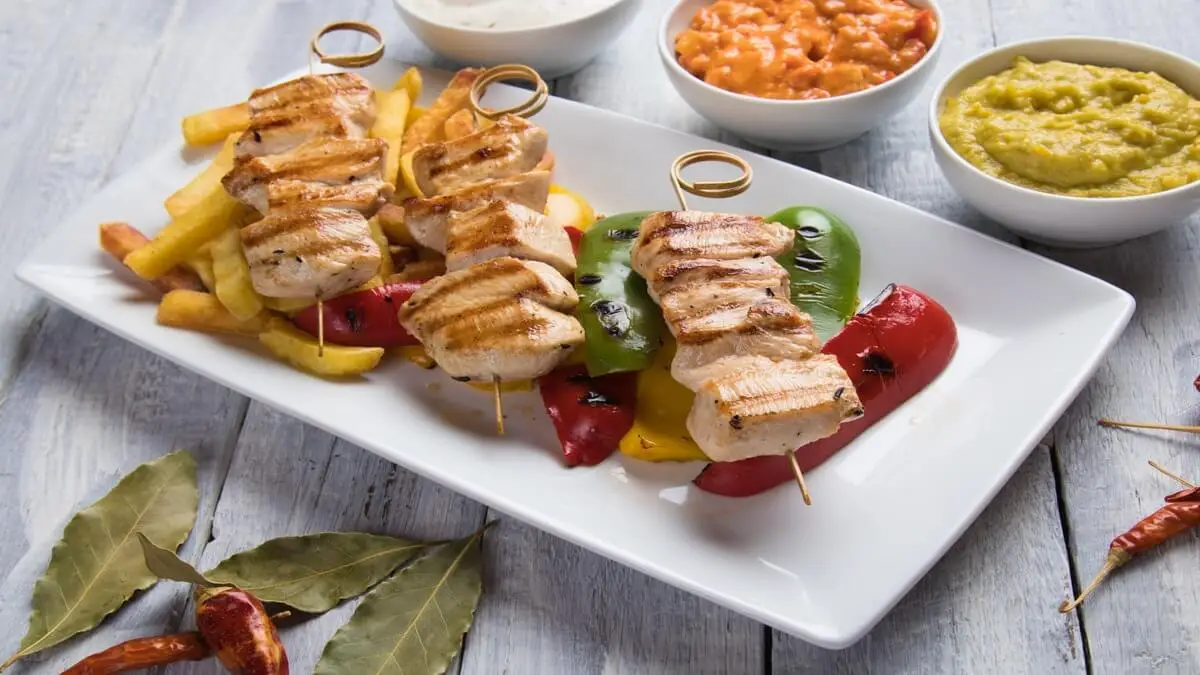 Brochetas de pavo sobre un plato, con patatas fritas y pimentones.