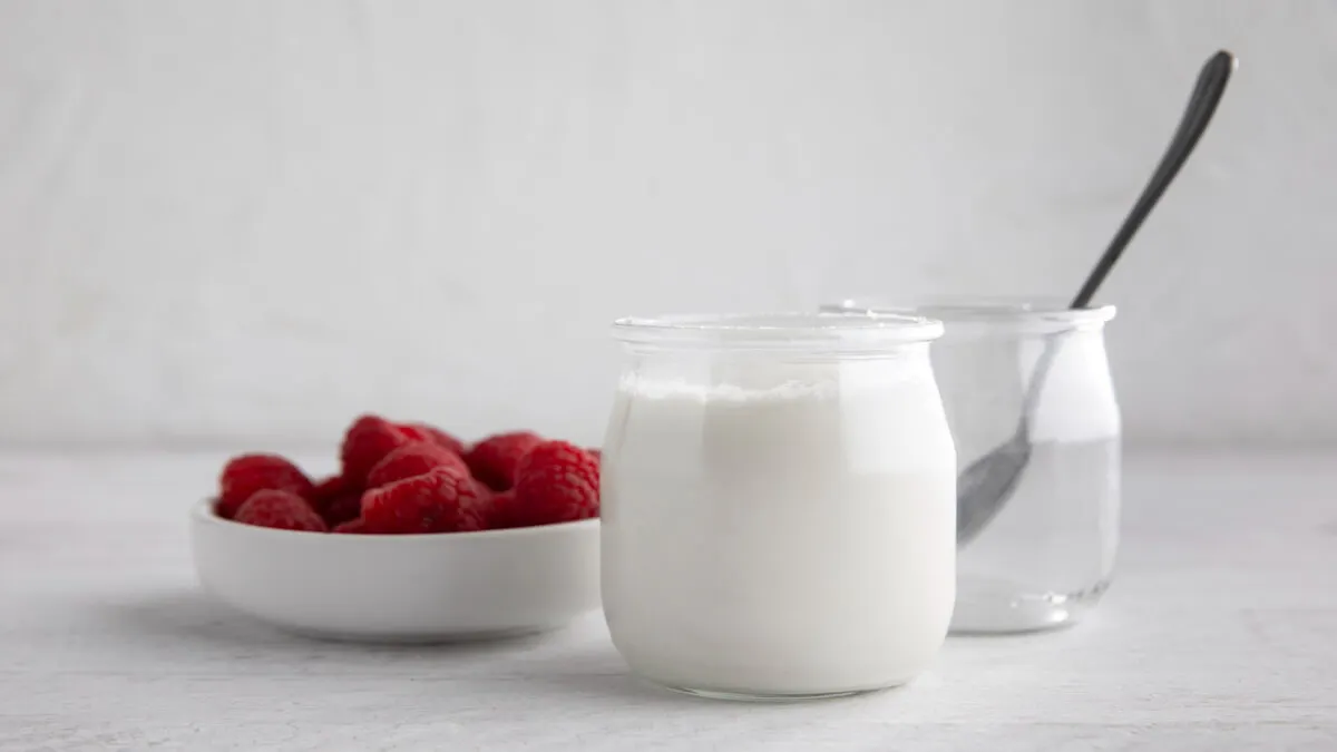 Dos vasos de yogur, junto a frambuesas.