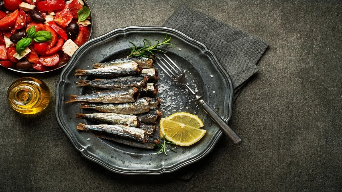 Sardinas sin cabezas sobre un plato, junto a un tenedor y limón.