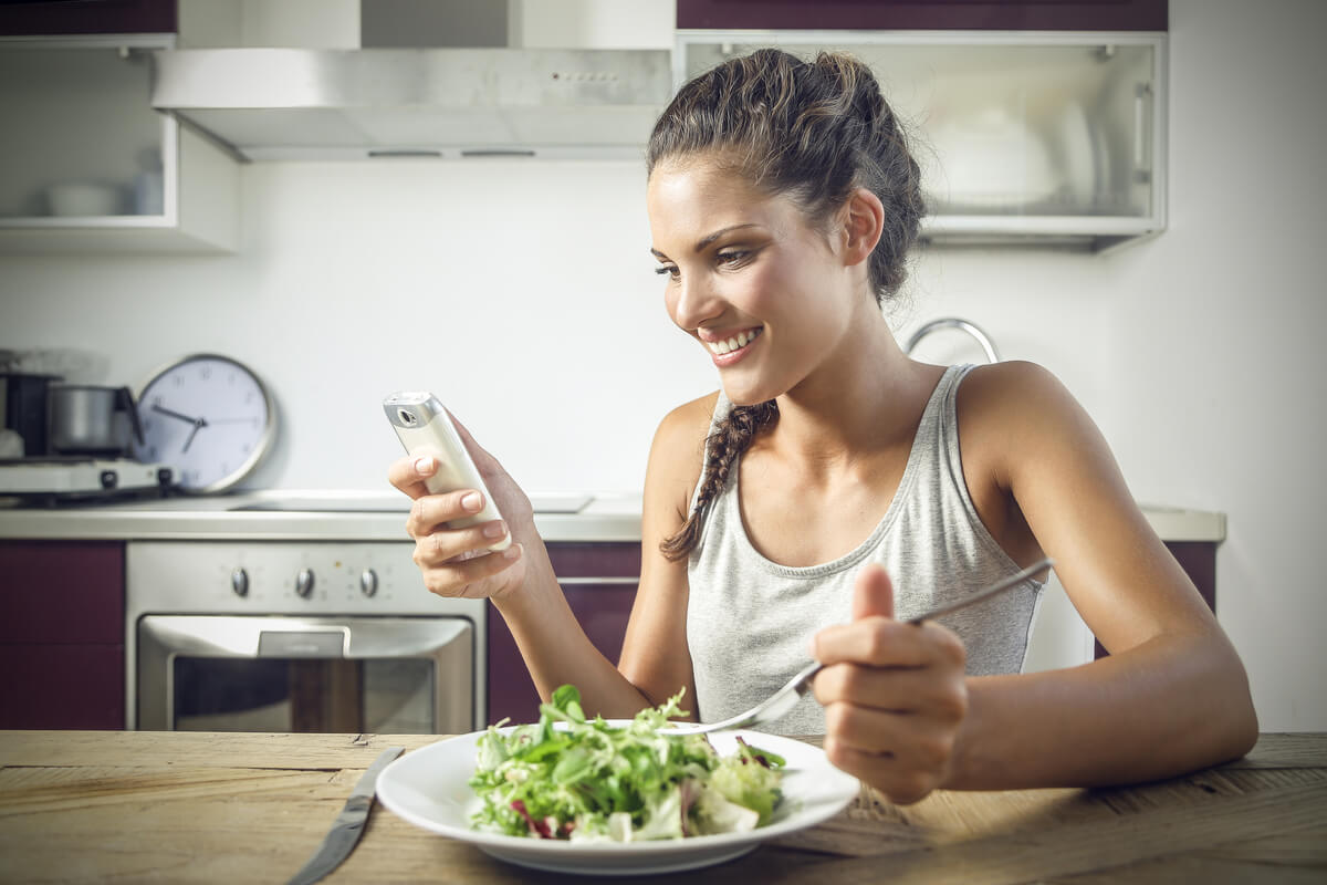 TikTok-Diätvideos - Frau isst Salat und schaut in ihr Smartphone