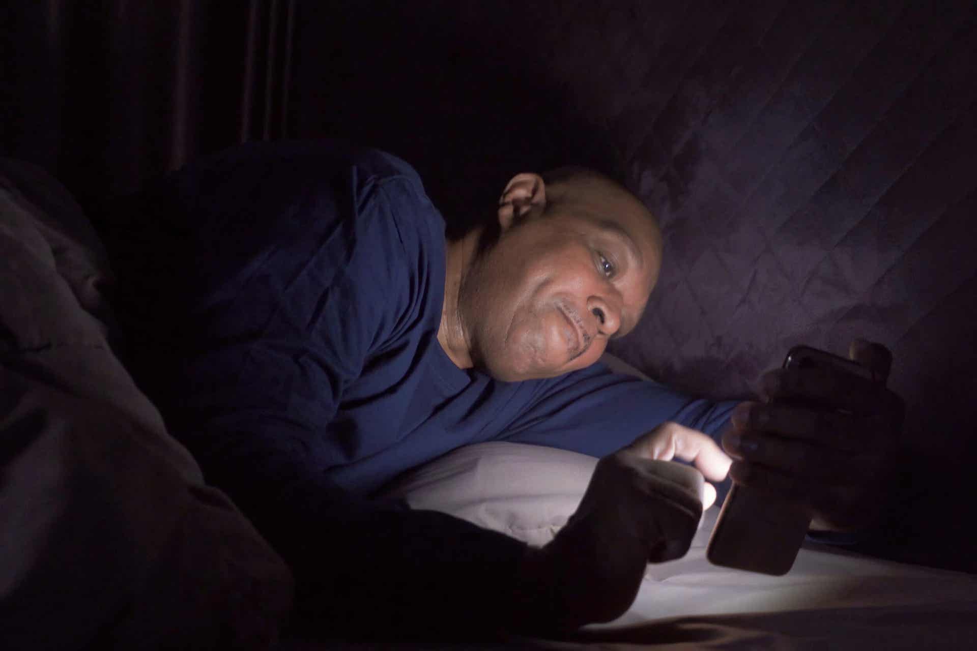 Man in bed druk bezig op zijn mobieltje