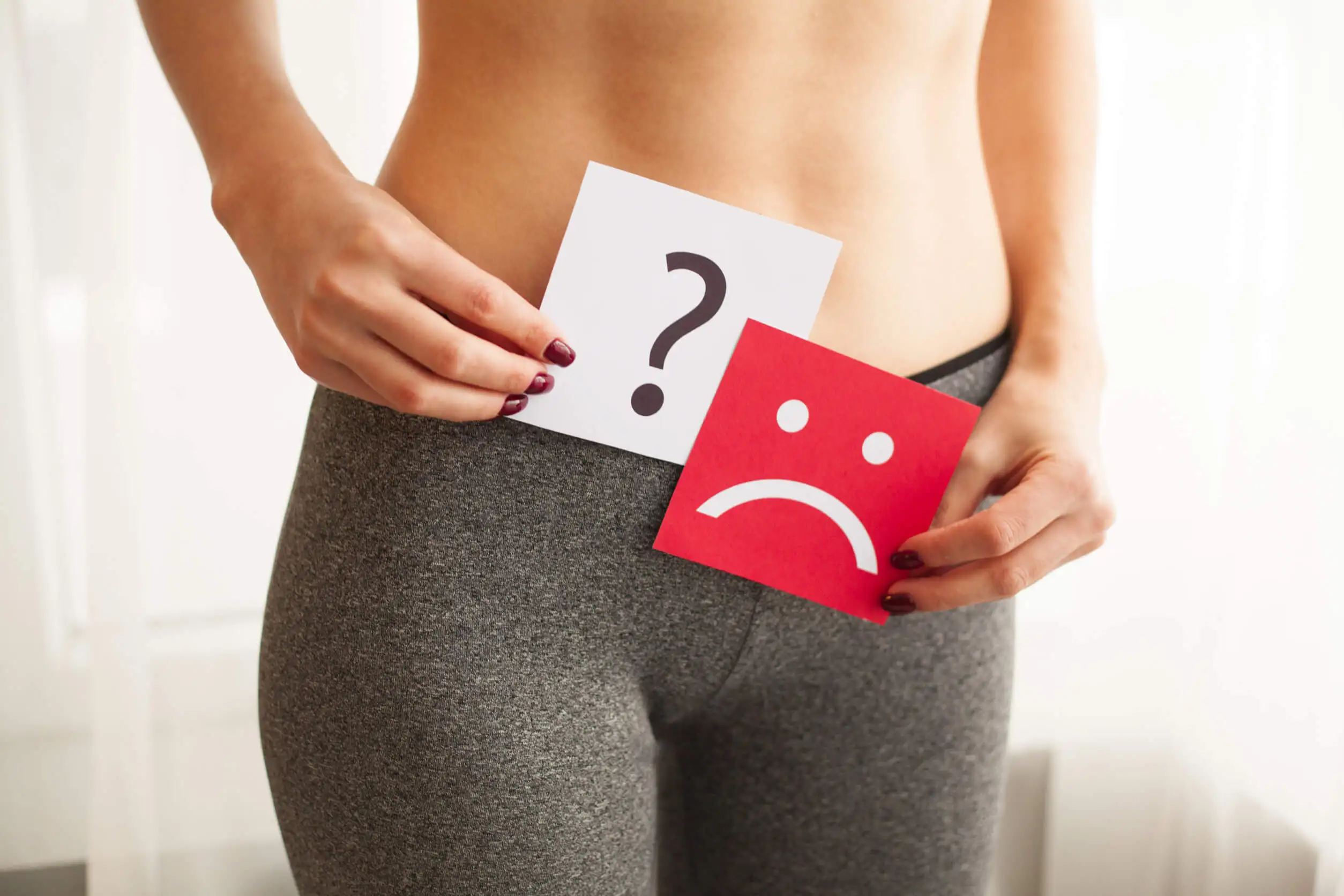 Kvinde med spørgsmålstegn og trist smiley foran underliv repræsenterer de forskellige typer af vaginal lugt