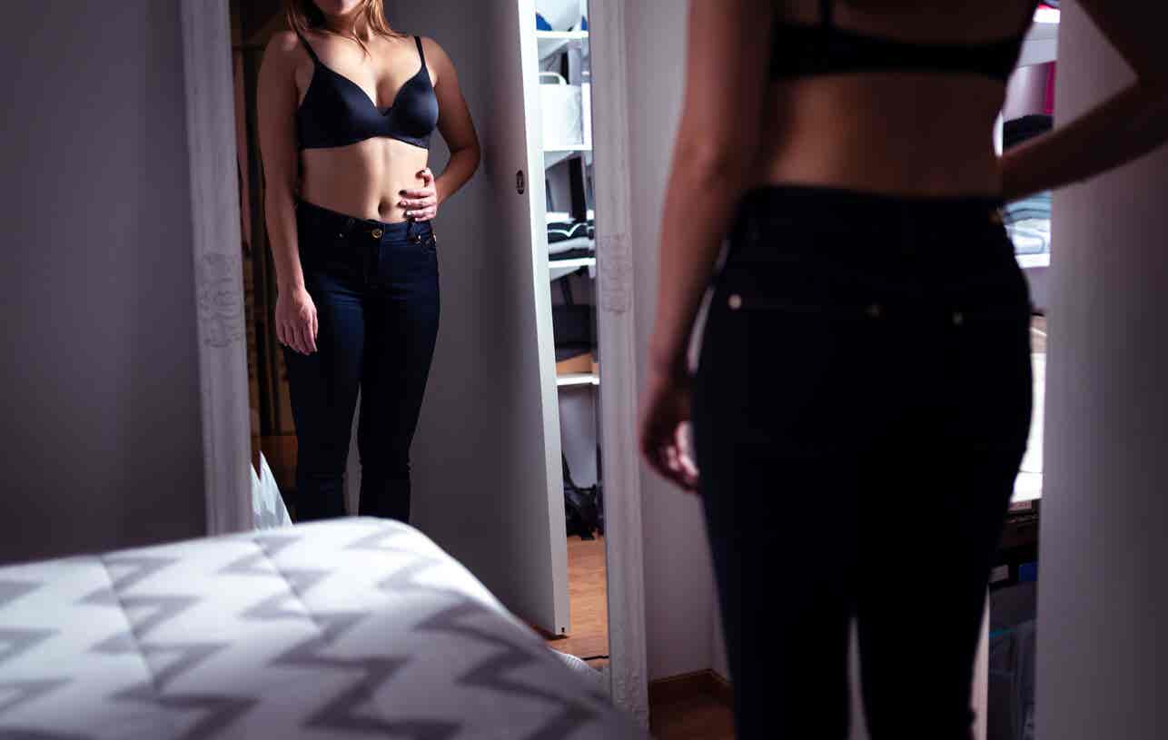 Mujer con obesofobia se mira al espejo.