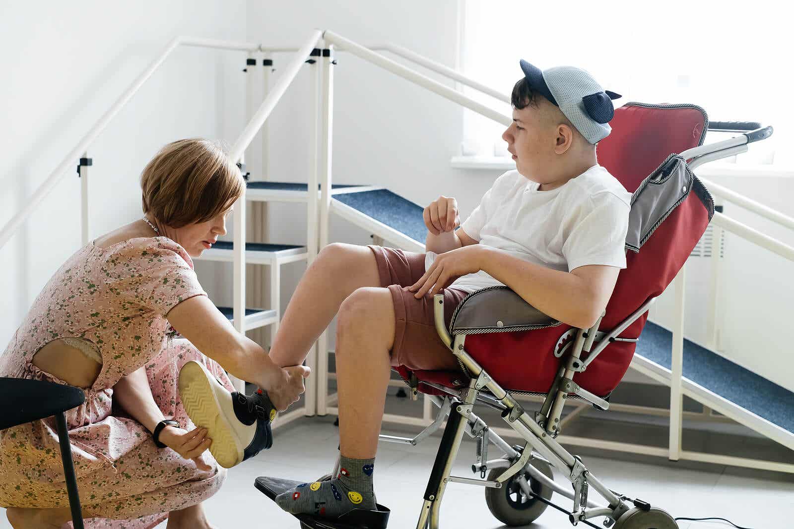 Physiotherapie bei Zerebralparese - Mutter zieht ihrem Sohn, der im Rollstuhl sitzt, die Schuhe an