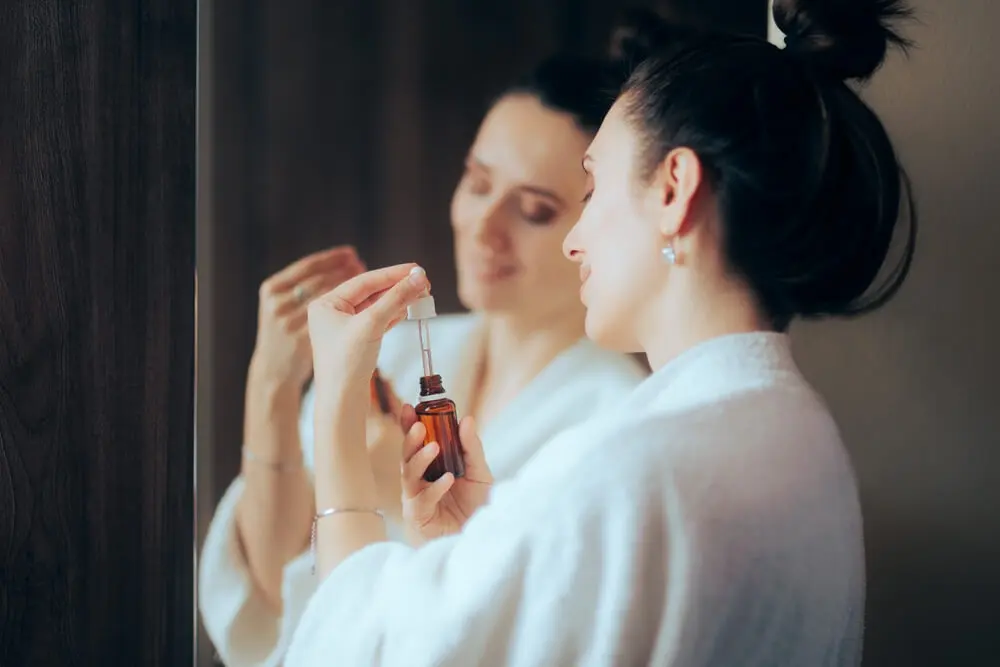 Melatonin-Seren - Frau mit einem Serum vor dem Spiegel