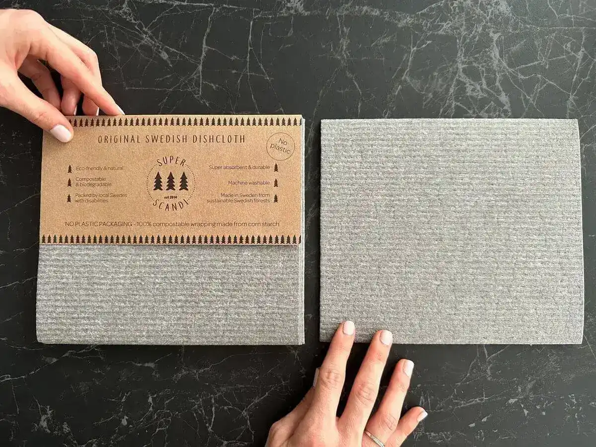 Paño de cocina sueco eco-friendly sobre encimera de mármol con embalaje de cartón que resalta características como biodegradable, compostable y sin plástico
