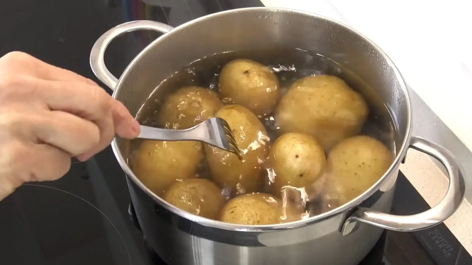 Una persona inserta un palillo en una papa que hierve en una olla junta a otras.