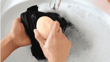 Persona frontando una prenda de ropa con una pastilla de jabón