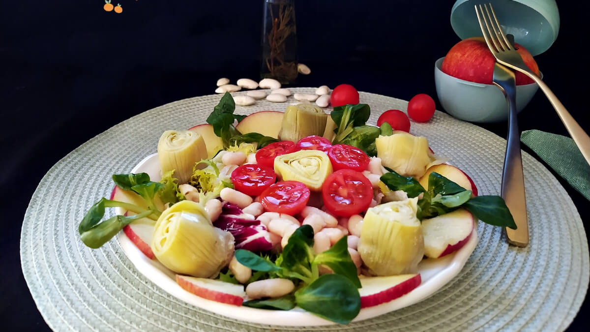 Plato de ensalada de alubias con manzanas sobre un individual.