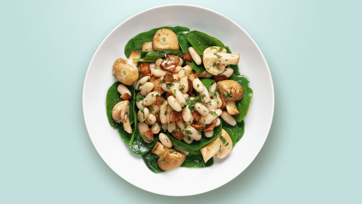 Ensalada de alubias con champiñones y espinacas sobre un plato blanco.