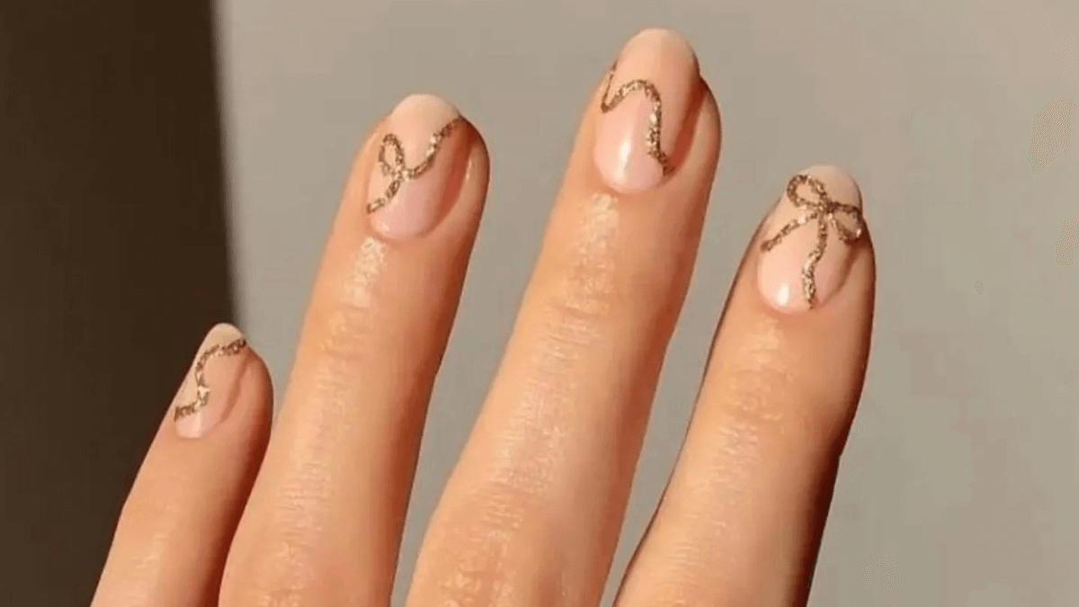 Unhas curtas com base nude e laços dourados.