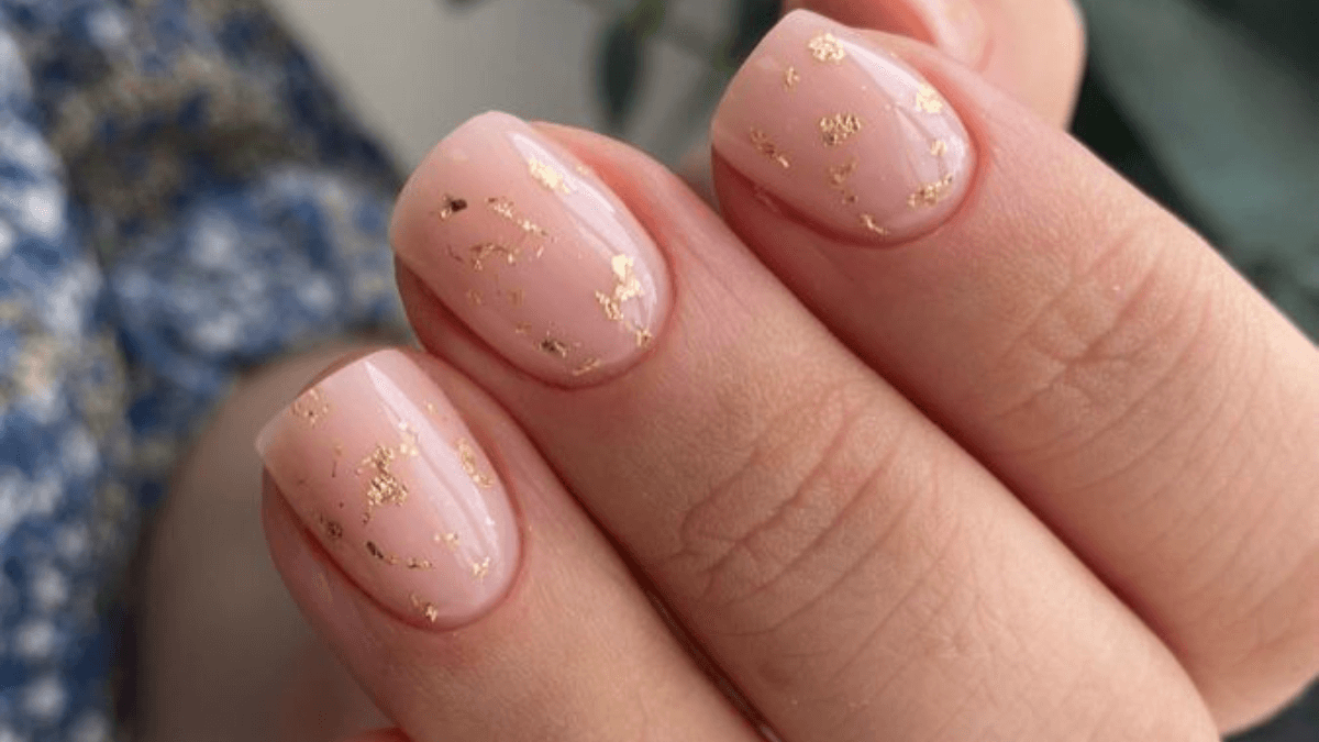 Unhas de base nude com toques de ouro.