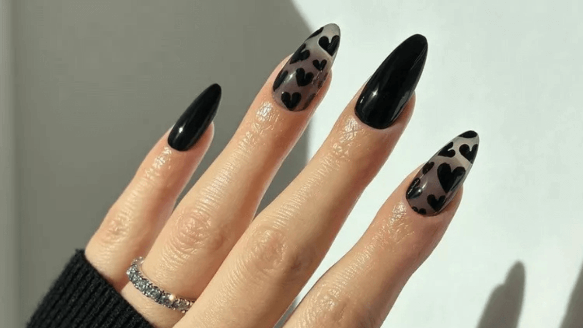 Uñas negras con detalles de corazones en dos dedos.