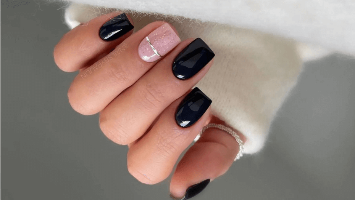 Uñas negras con dedo anular en rosa y detalle plateado.