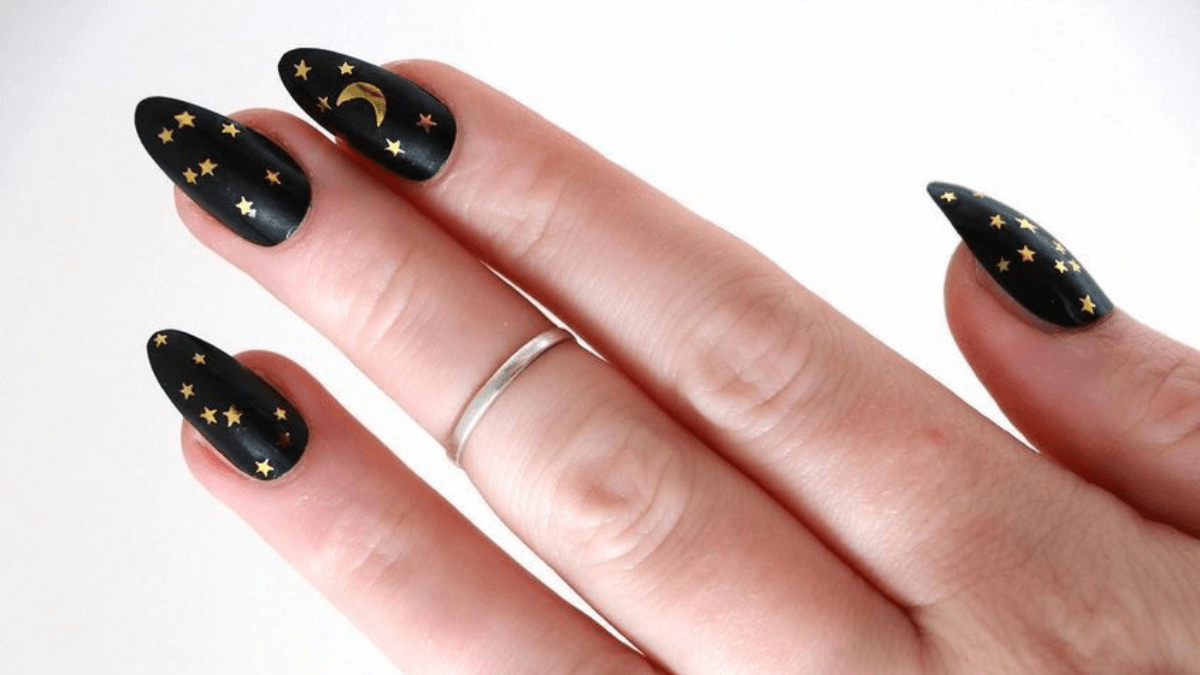 Uñas con fondo negro con estrellas y lunas encima.