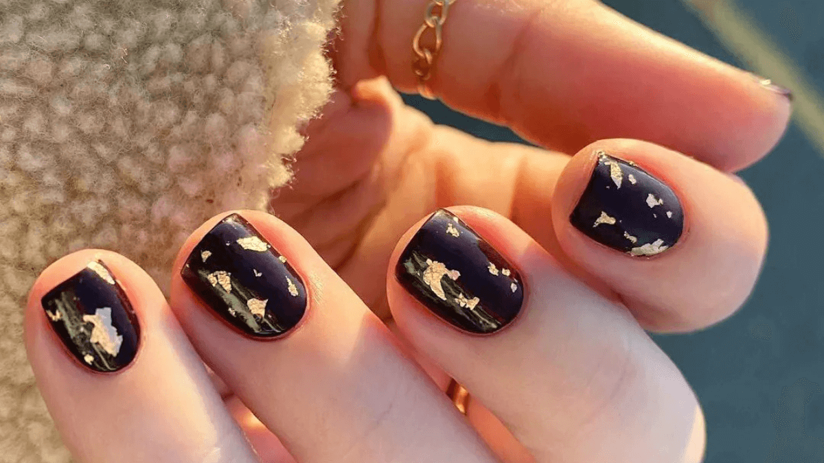 Uñas pintadas de negro con detalles en dorado.