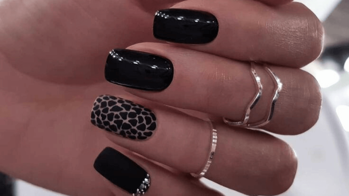 Uñas negras con el diseño de leopardo en el dedo anular.