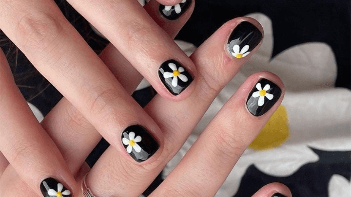 Uñas negras con detalles de margaritas blancas.
