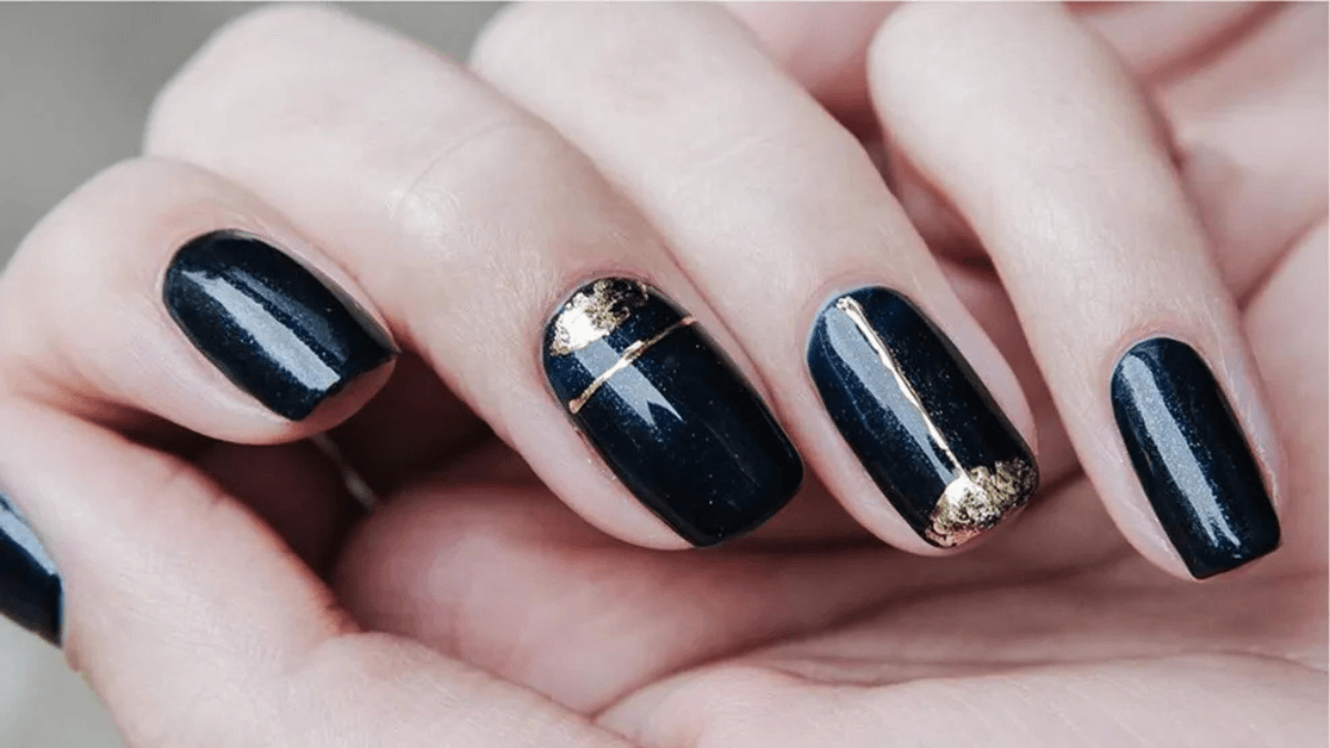 Uñas pintadas de negro con detalles en dorado en el dedo anular y medio.
