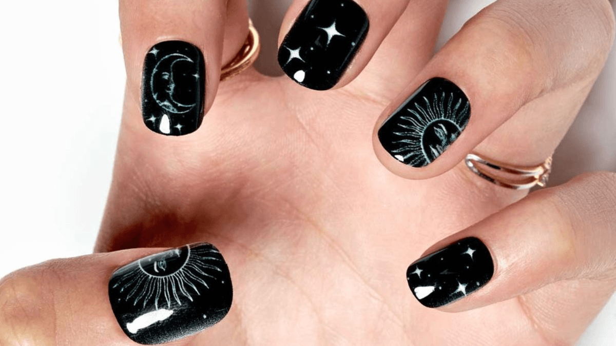 Uñas negras con detalles de luna, sol y estrellas.