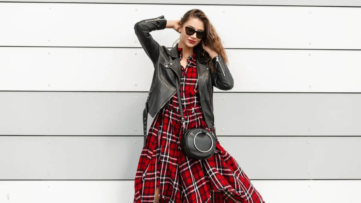 Mujer luce vestido con estampado escocés y chaqueta de cuero.