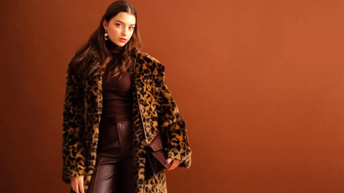 Mujer con chaqueta de animal print, franela y pantalón marrón.
