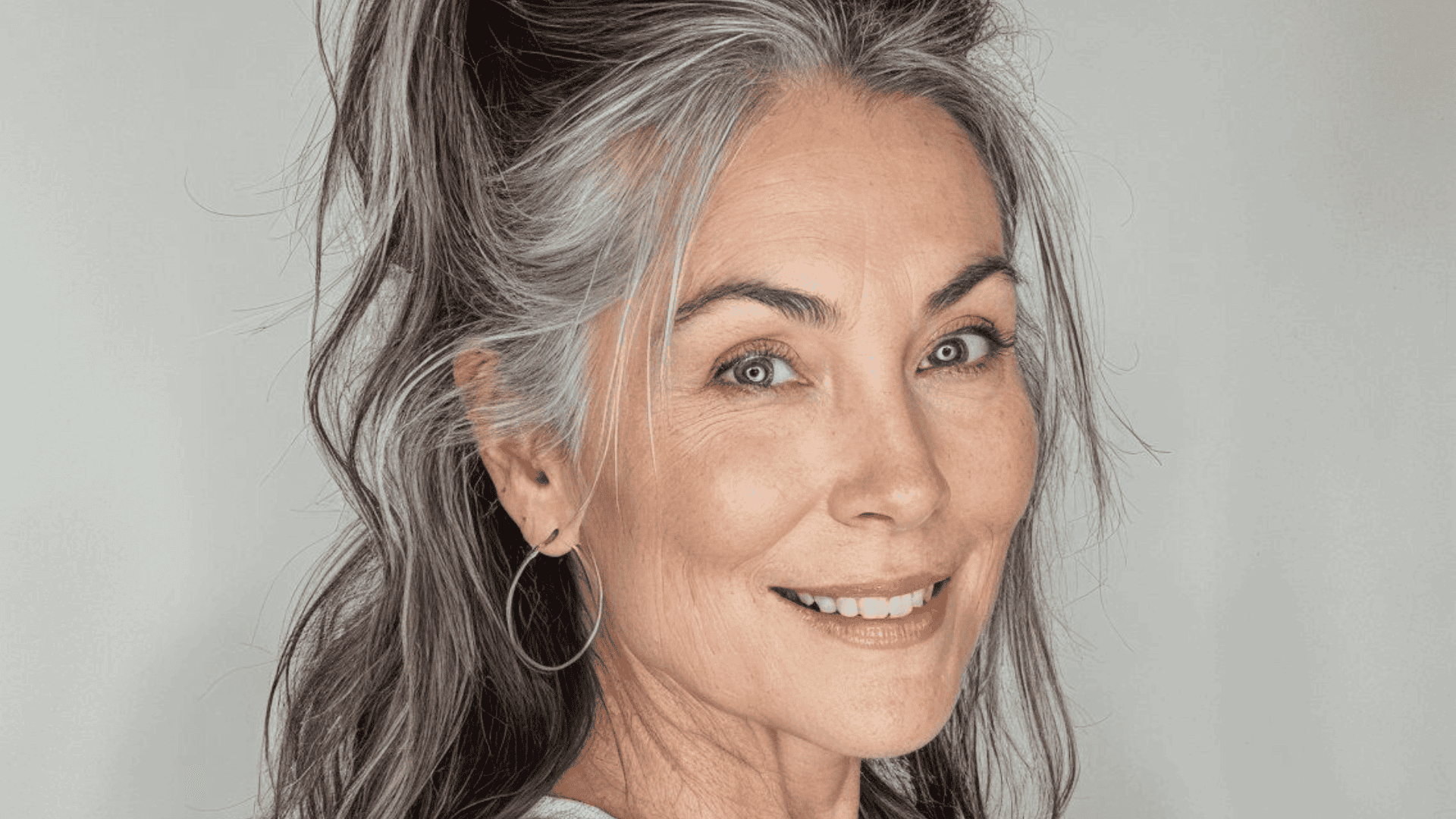 Mujer con canas luce coleta alta.