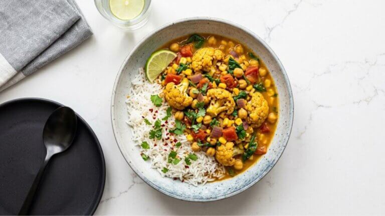 Curry de coliflor, garbanzos, tomate y maíz servido con arroz