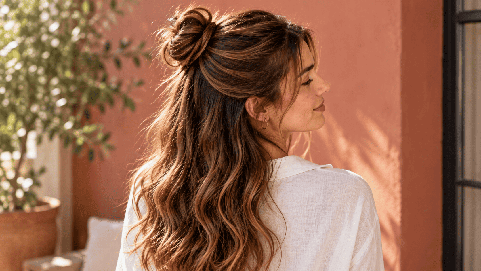 Mujer con moño semirrecogido alto, cabello castaño ondulado y mechones sueltos sobre la espalda.